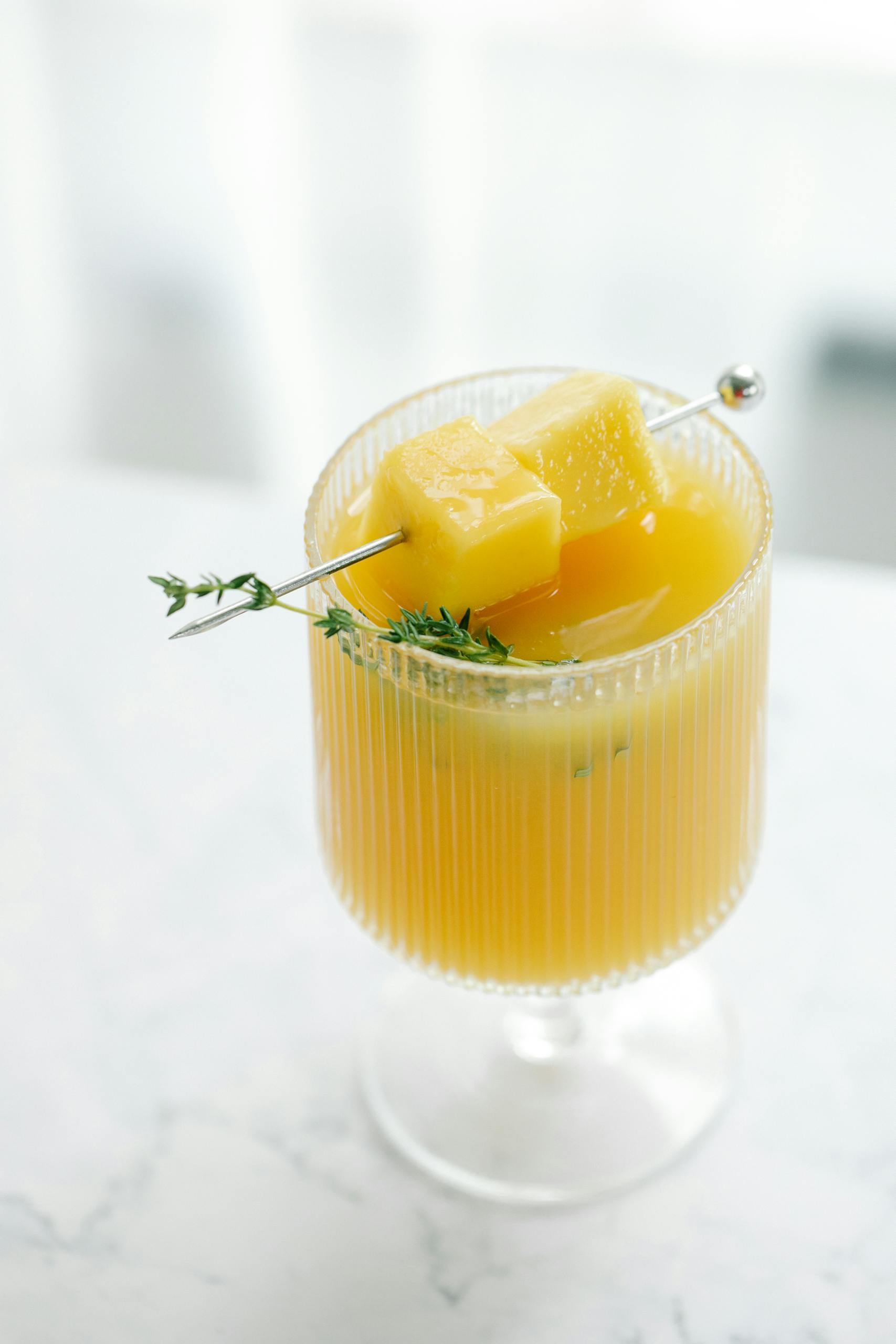 A refreshing pineapple cocktail with herb garnish served in a clear glass on a table.